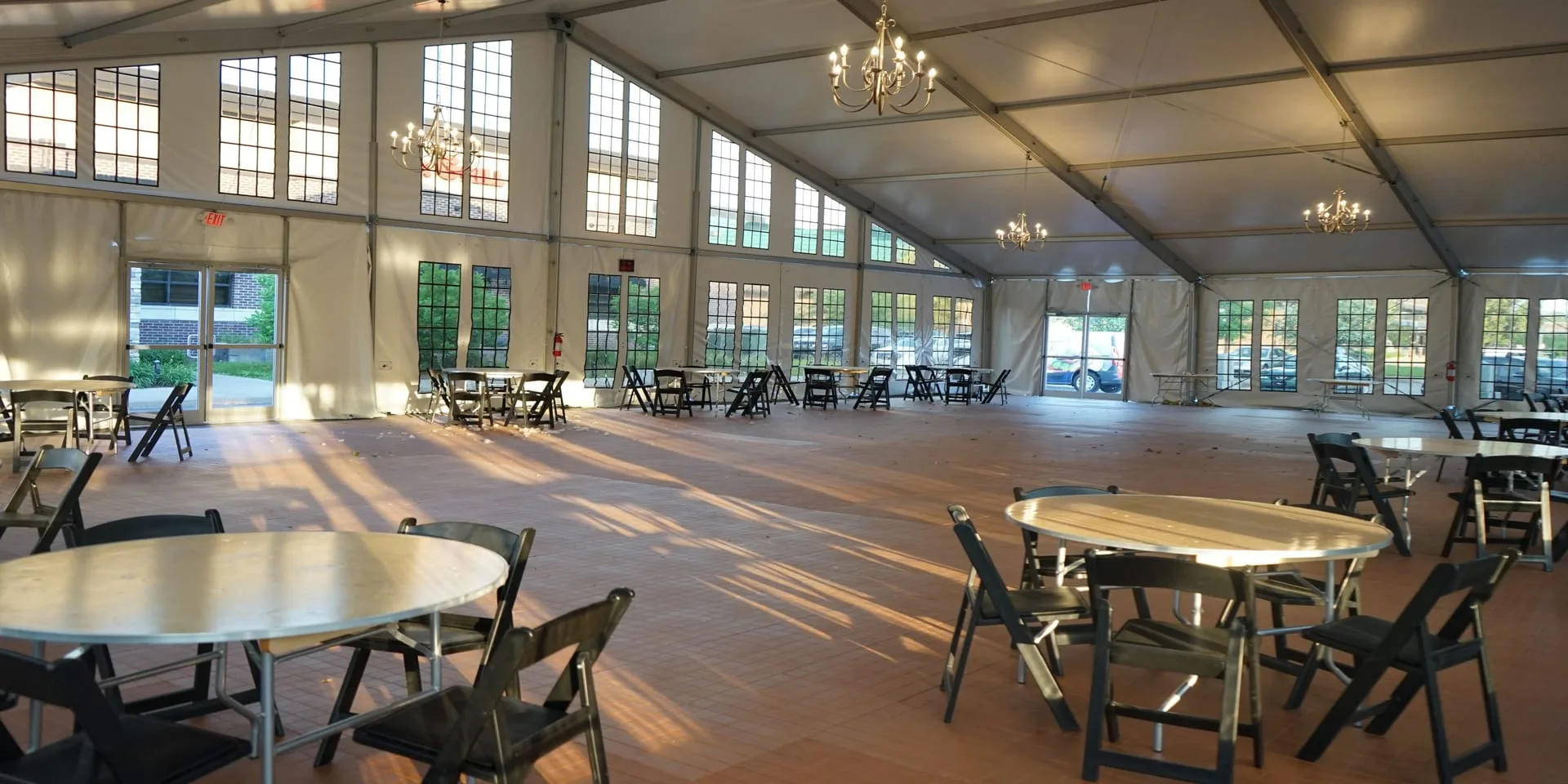 Glass wall structure tent interior with chandeliers, wood flooring, and round tables